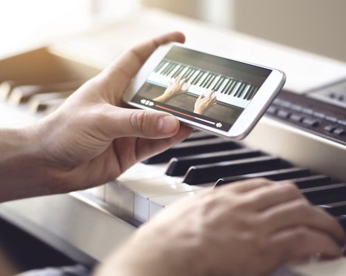 Piano lesson online. Man watching video tutorial with mobile phone and practising playing. Person learning to play an instrument with an internet course and class. Pianist training with smartphone.